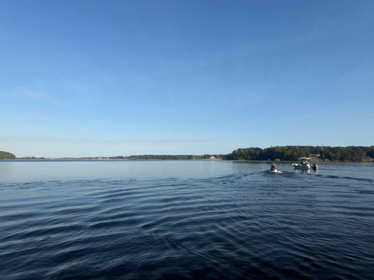 A jet ski and a boat on Roanoke Rapids Lake with the wooded shoreline in the distance
