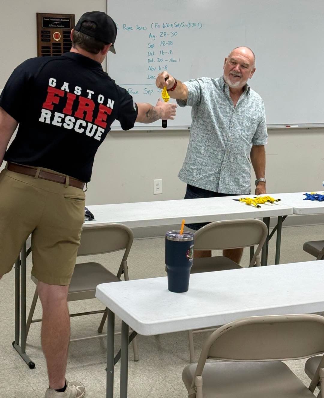 A Gaston member reaching across a table to receive a yellow knot from the instructor