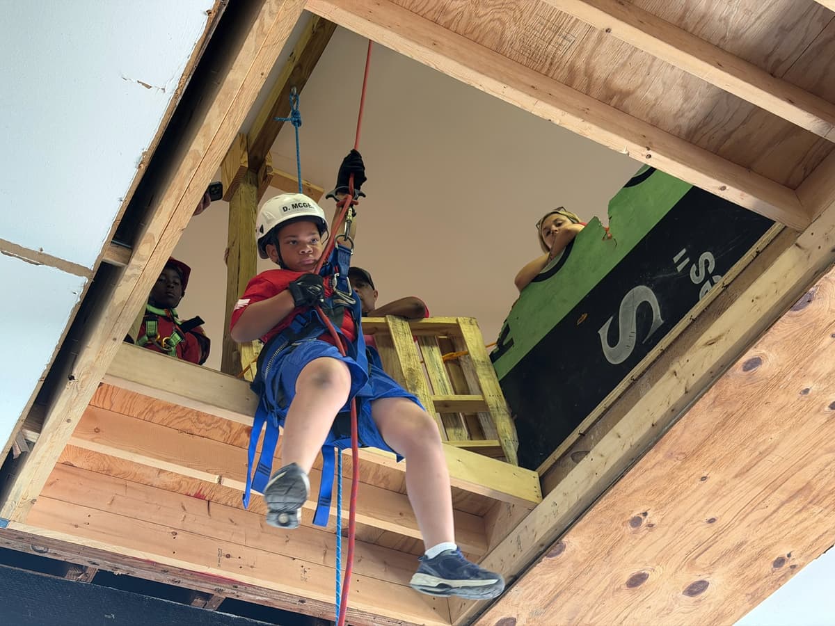 A camper rappels from the training loft in a helmet and harness