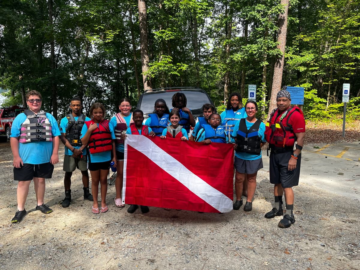 Campers in life jackets gather with a diver-down flag